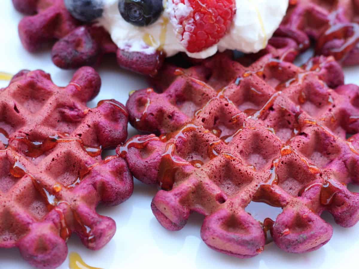 Red beetroot waffles drizzled with syrup and topped with yogurt and berries. 