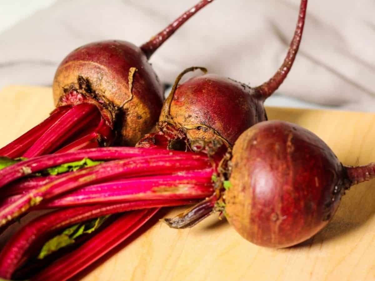Fresh beetroots with green stems/greens on a cutting board. 