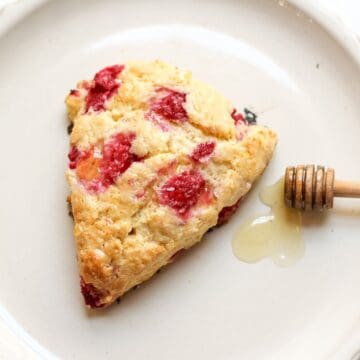 Golden brown raspberry honey scone with fresh berries and a glossy honey drizzle on a plate.