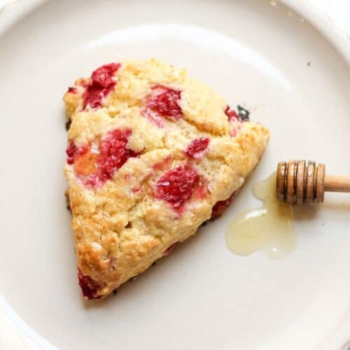 Golden brown raspberry honey scone with fresh berries and a glossy honey drizzle on a plate.