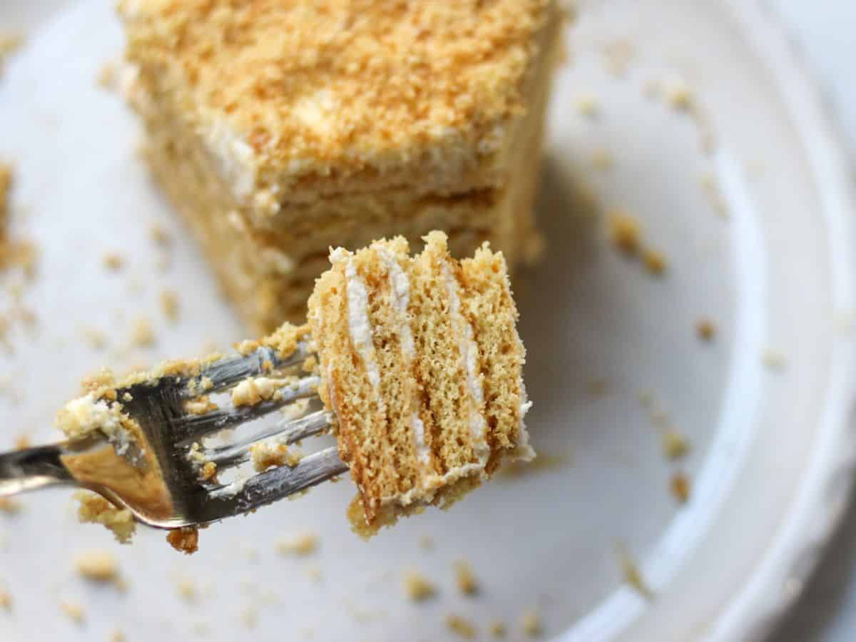 Close-up of a piece of medovik cake on a fork showing the soft layers with sour cream frosting. 