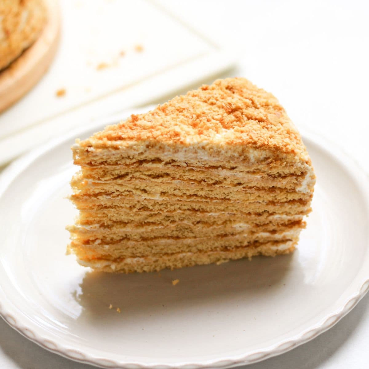 Authentic 8-layer Medovik honey cake on a white plate, showing the soft hydrated layers, sour cream frosting, and a signature golden crumb coating.