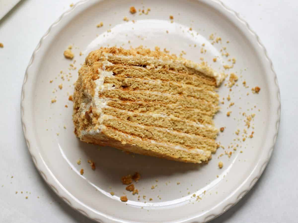 A slice of 8-layer medovik honey cake with soft honey layers and creamy sour cream frosting, served on a plate.  