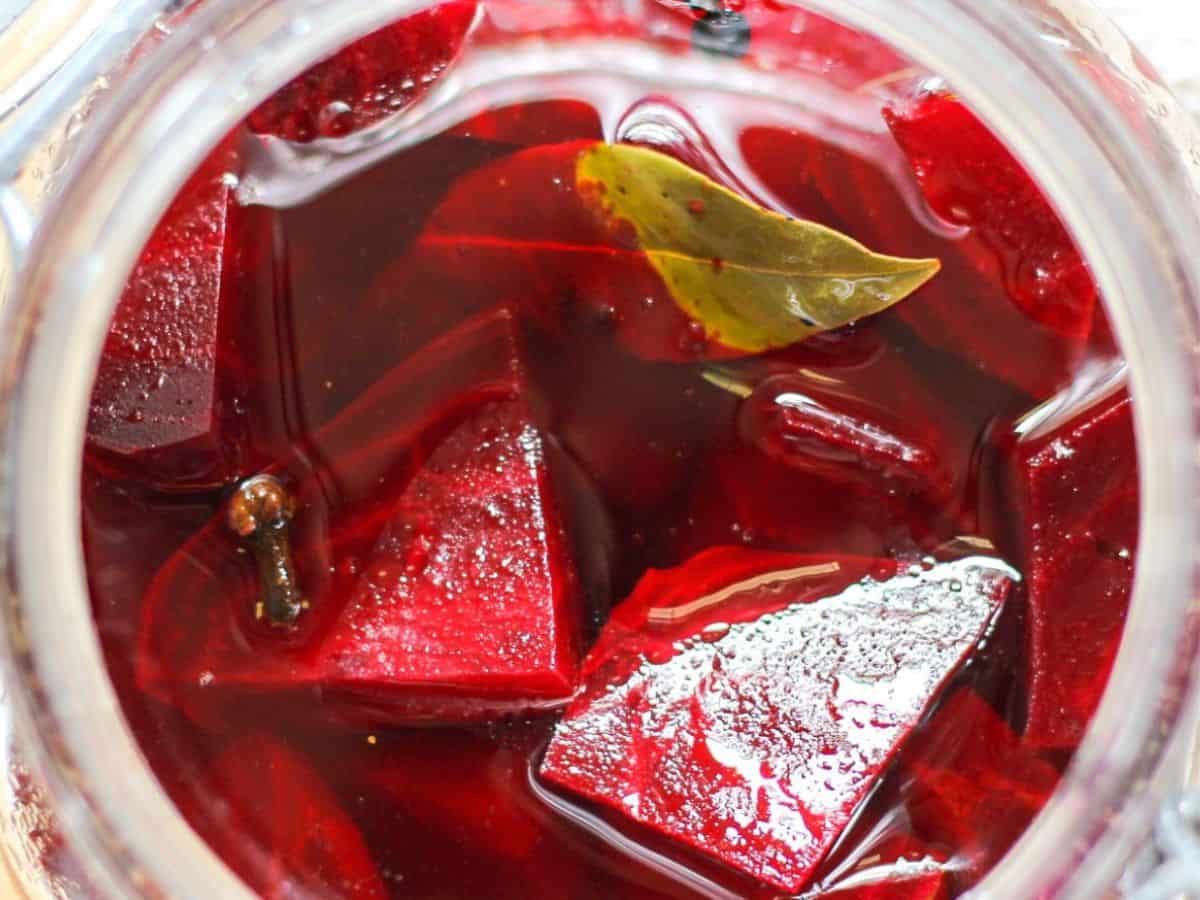 Refrigerator pickled beet pieces in a jar with bay leaves and whole peppercorns. 