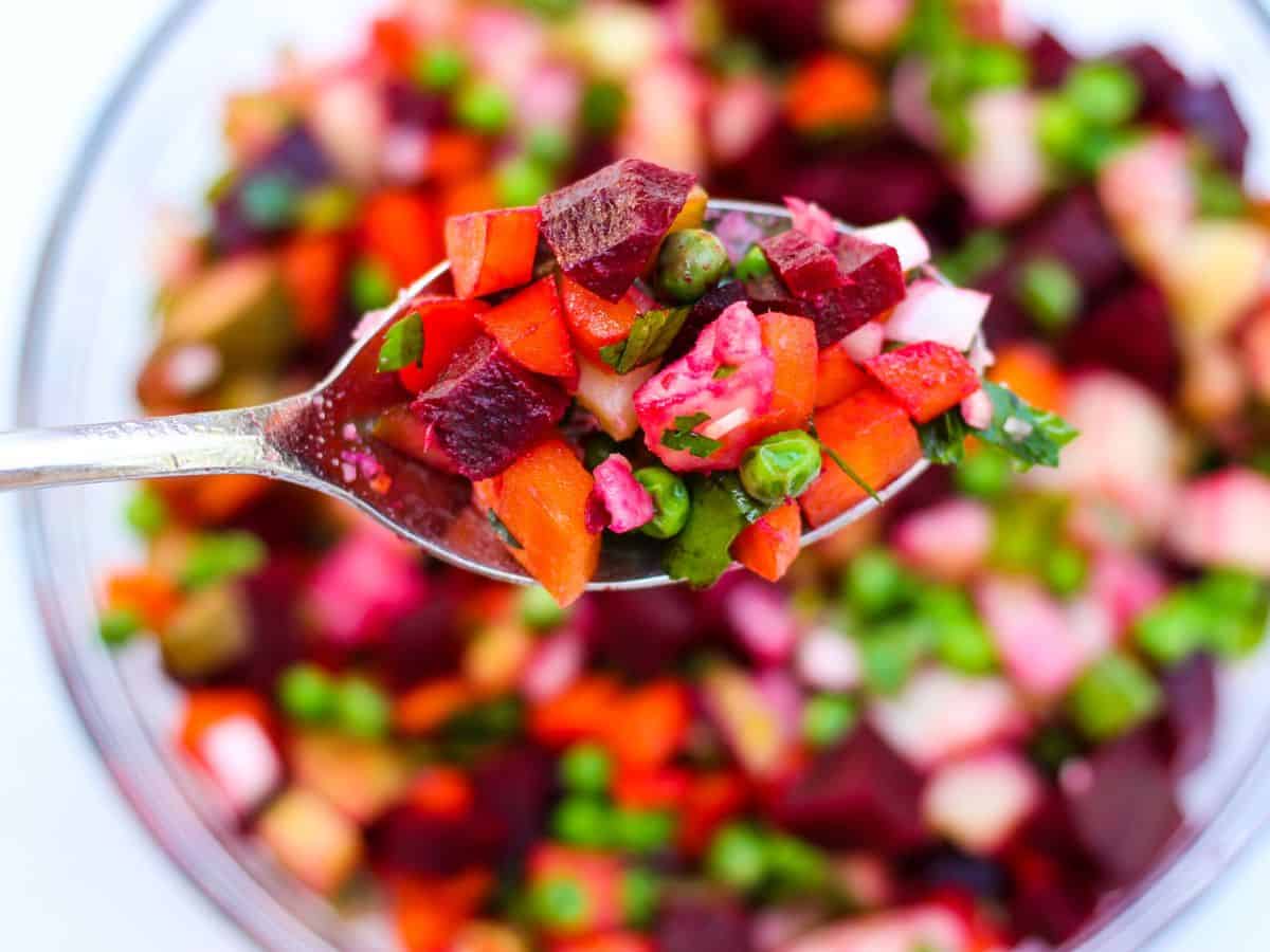 A spoonful of vinegret salad made with diced beets, potatoes, carrots, pickles and peas. 
