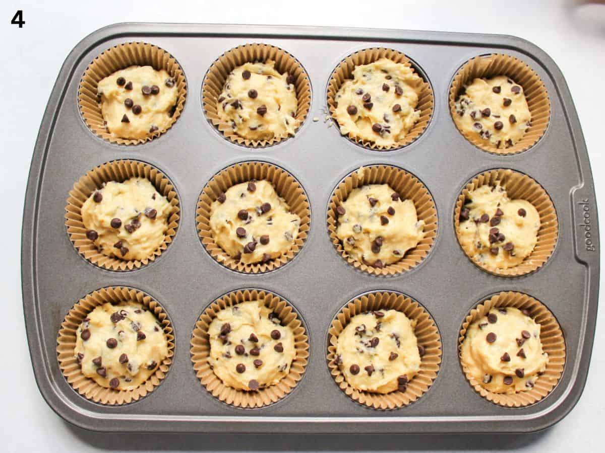 A 12-cup muffin tin filled with sour cream chocolate chip muffin batter, topped with extra chocolate chips. 