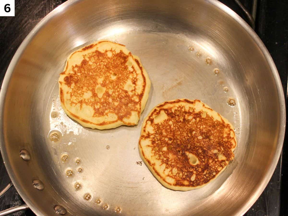 Golden-brown pancakes cooking on the skillet after flipping.