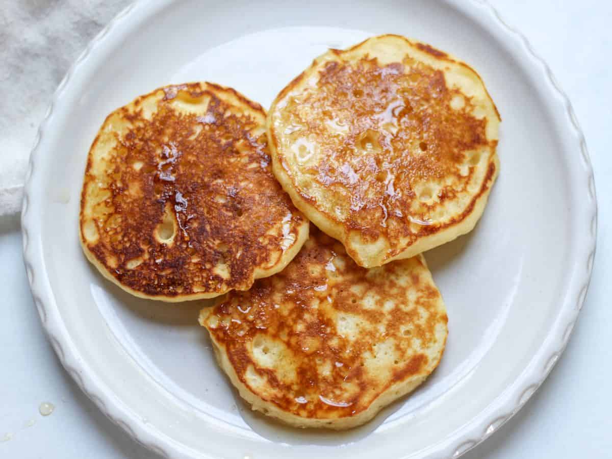 Three fluffy pancakes, drizzled with maple syrup and served on a plate.