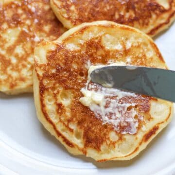 Fluffy American pancakes, served on a plate, drizzled with warm maple syrup, and spread with butter.