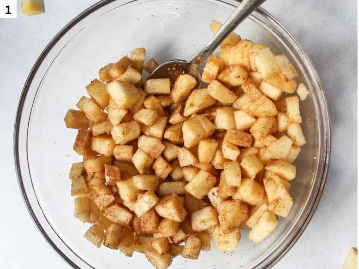Diced apples tossed with cinnamon, nutmeg, cardamom and sugar in a glass bowl. 