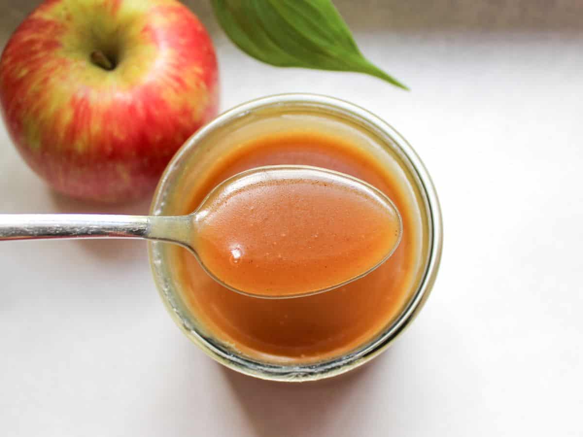 Apple cider caramel sauce in a glass jar, with a spoonful holding over it. 