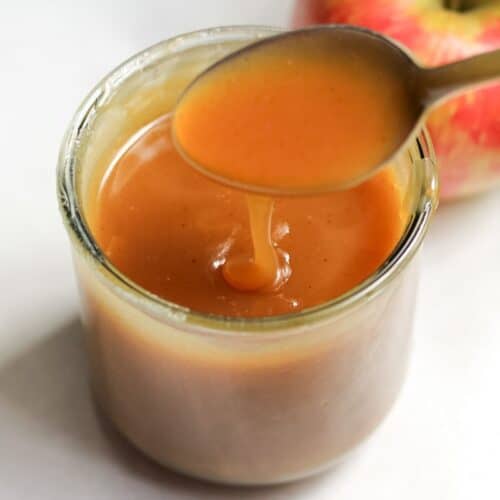 Apple cider caramel sauce in a jar with a spoonful dripping back into the jar.