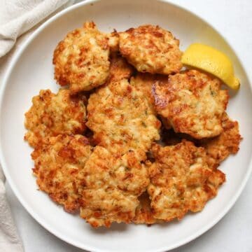 Golden crispy chicken fritters served on a plate with a fresh lemon wedge.