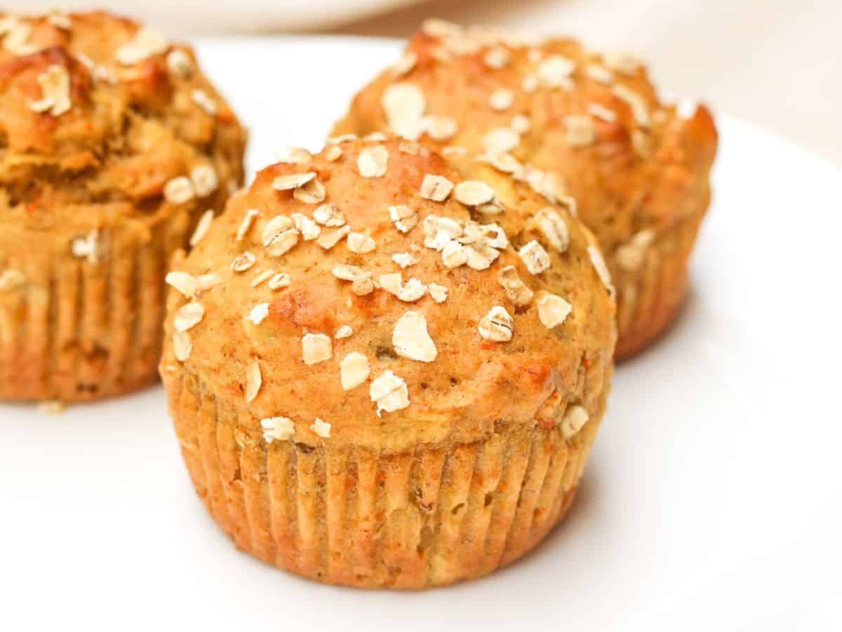 Honey apple banana carrot muffins with oat flakes topping served on a plate.