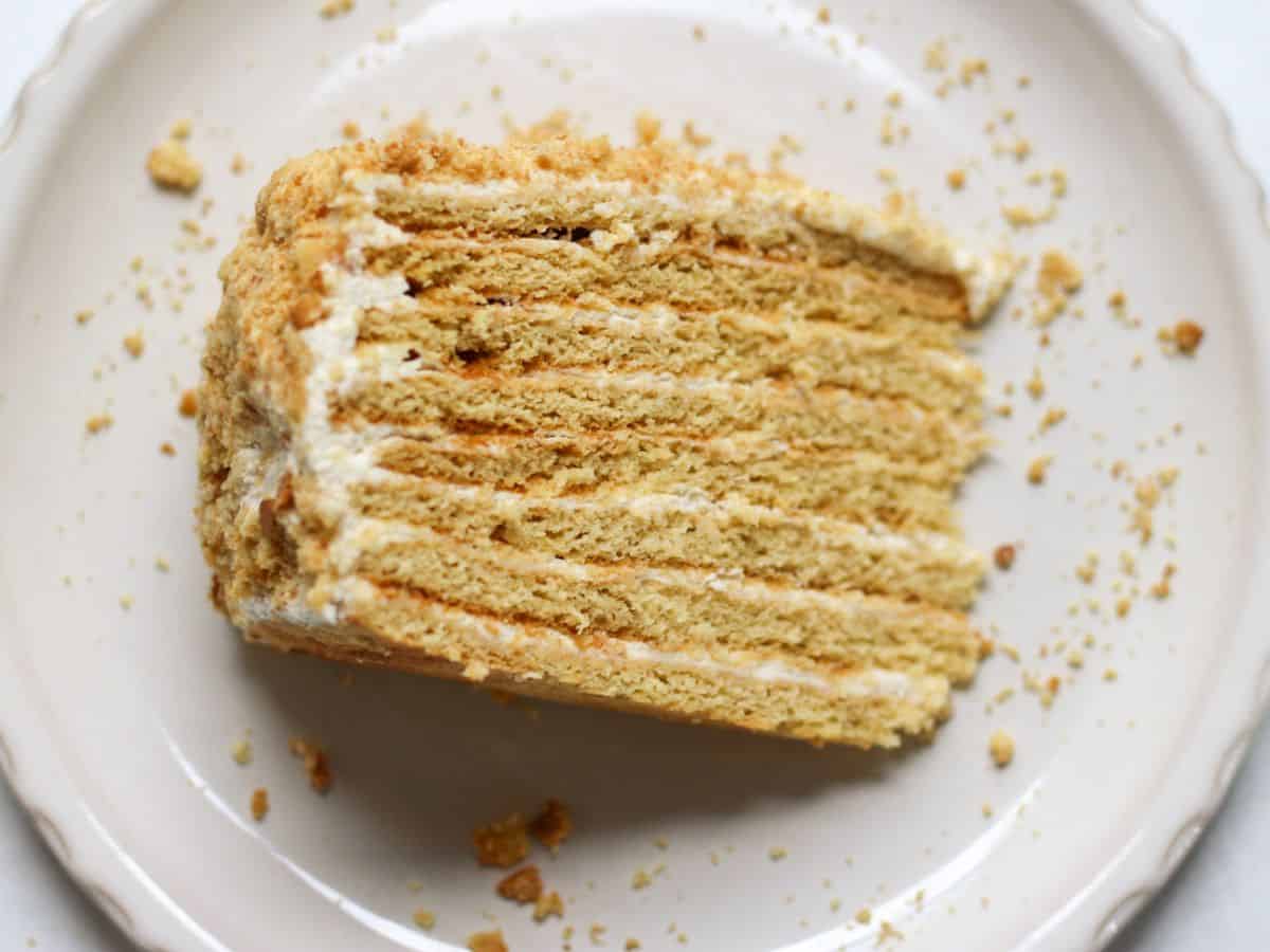 A slice of 8-layer Medovik cake with white frosting, served on a plate.