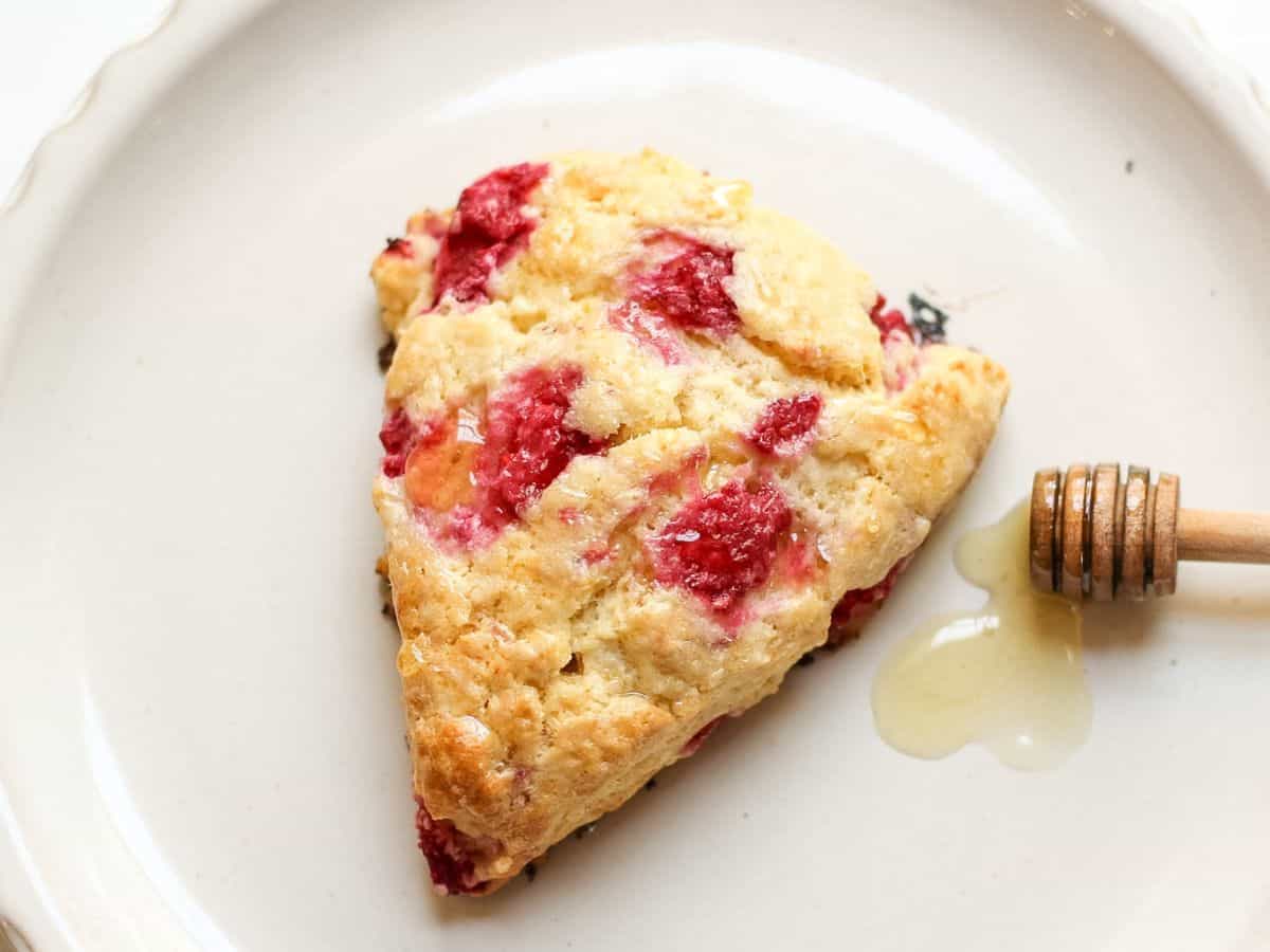 Honey scone with raspberries drizzled with honey, served on a plate.