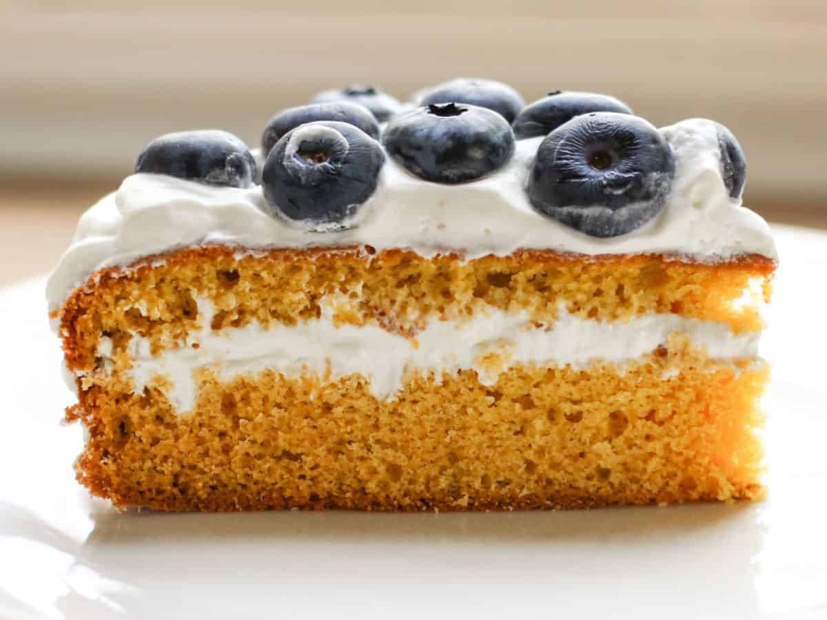 Honey sponge cake slice with white frosting and blueberries on top.