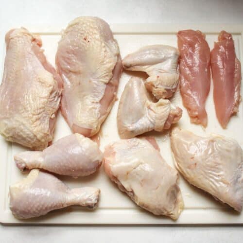 Chicken fresh chicken pieces on a cutting board after cutting a whole chicken, including 2 chicken breasts, 2 tenderloins, 2 wings, 2 drumsticks, and 2 thighs.